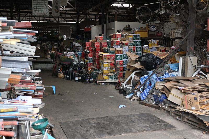 This photo shows what appears to be a cluttered storage or warehouse space. There are stacks of cardboard boxes, including what look like beverage cartons (poss